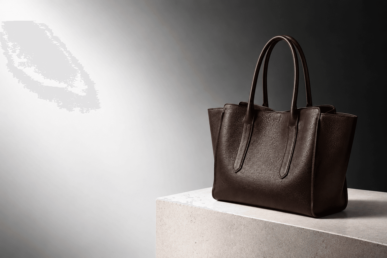 Espresso leather tote on a warm stone plinth